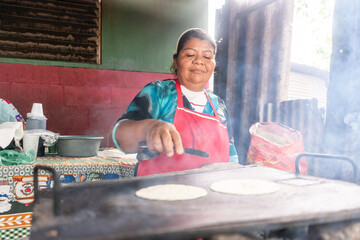 Humble woman from Nicaragua preparing tortillas on a metal griddle. Latin American people in their daily lives - obrazy, fototapety, plakaty
