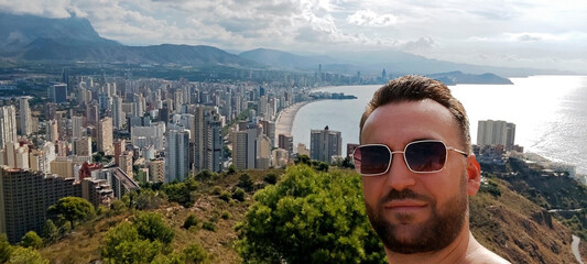 Man taking a selfie with a selfie stick with the cityscape in the background. Benidorm, Spain.