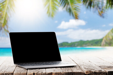 Laptop with blank screen on wooden table in front of sunny sea
