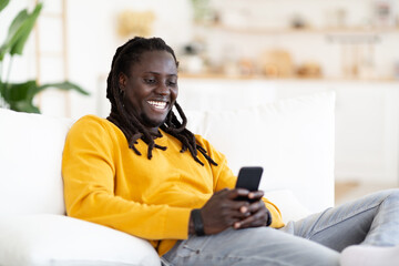 Mobile Messaging. Black Guy Using Smartphone While Resting In Chair At Home