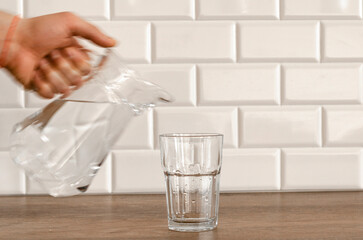 A man's hand pouring fresh pure water from bottle into a glass on the table, health and diet concept