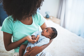 half Nigeria half Thai, 1-month-old baby newborn son, looking at mother while his mother being held and sitting on a white bed, to relationship in family and infant newborn concept.