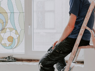 A young caucasian tired from work guy sits and rests on a dirty stepladder