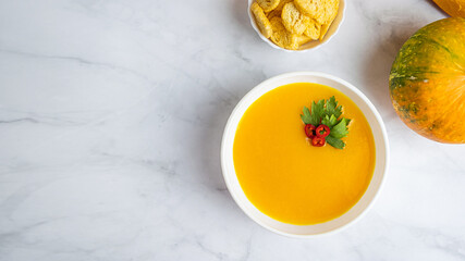 Autumn pumpkin cream soup with pumpkin spices. Delicious and bright vegetarian dish with foodstyling of fresh parsley with hot pepper and seasonings on a white background. Banner with copy space text