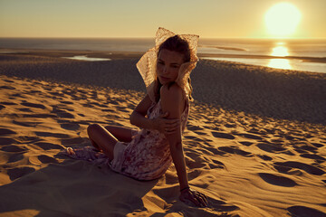 Lovely photo of young woman sitting on the sand at sunset with golden sky