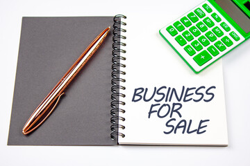 Business for sale word on a notepad with a calculator and a pen. Concept of preparing a business for resale, business development.