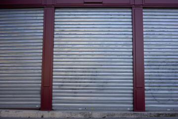 Three large silver metal gates are closed. Front view of a purple building with a sidewalk in the foreground. House facade in an industrial area