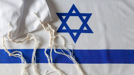 The tallit katan (Hebrew tallis koton, small tallit) with the flag of Israel background. Tallith katan - cape with brushes. Traditions, ritual object. Jewish holiday of Sukkot, shabbat, rosh hashanah