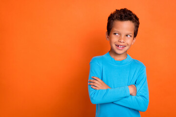 Photo of cheerful nice boy arm folded look empty space plan idea dressed blue stylish pullover isolated on orange color background