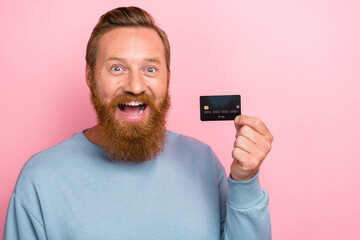 Photo of handsome impressed positive guy red beard wear blue long sleeve excited hold plastic card isolated on pink color background