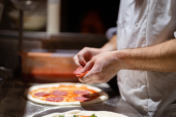 Pizza making process. Male chef hands making authentic pizza in the pizzeria kitchen.