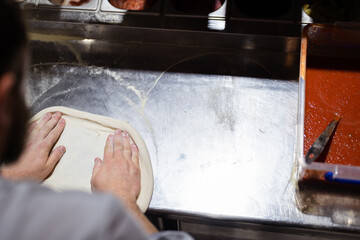 Fototapeta na wymiar Pizza making process. Male chef hands making authentic pizza in the pizzeria kitchen.