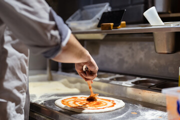 Pizza making process. Male chef hands making authentic pizza in the pizzeria kitchen.