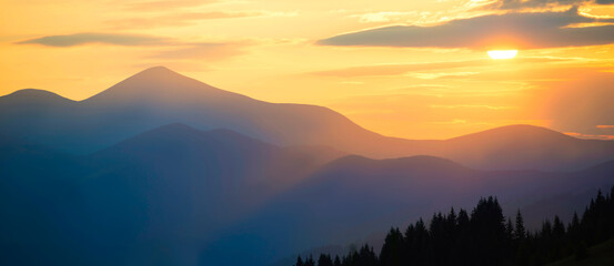 Sunset in mountains. Panorama mountains landscape with sun shining through orange clouds