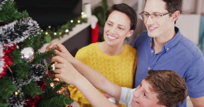 Happy caucasian parents and son decorating christmas tree at christmas