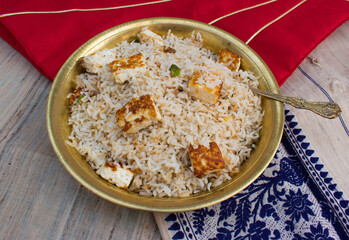 Homemade healthy paneer herb rice or pulav or fried rice in yellow brass plate and spoon with red and blue background.