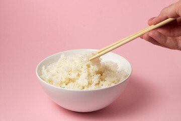 The hand takes the boiled rice with chopsticks on a pink background. Traditional Asian food.