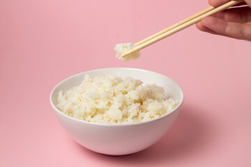 The hand takes the boiled rice with chopsticks on a pink background. Traditional Asian food.