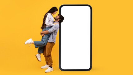 Loving indian couple posing near big blank smartphone with white screen