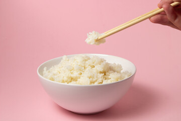 The hand takes the boiled rice with chopsticks on a pink background. Traditional Asian food.