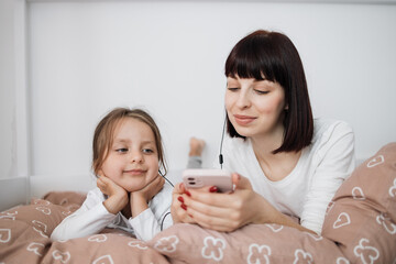 Obraz na płótnie Canvas Close up of smiling mom and little daughter relax in cozy bed read funny interesting children book together, happy mother and small preschooler girl child enjoy fairytale rest in comfortable bedroom
