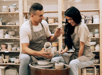 Couple in love working together on potter wheel in craft studio workshop.