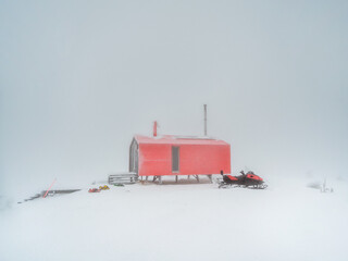 Soft focus. Poor visibility. Red house and a snowmobile on a foggy snow-covered mountain. Winter holidays, extreme adventures in winter.