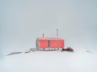 Fotobehang Soft focus. Poor visibility. Red house and a snowmobile on a foggy snow-covered mountain. Winter holidays, extreme adventures in winter. © sablinstanislav