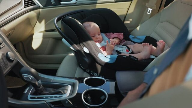 Father sitting in driver s seat. Smiling baby boy in child seat looking at dad. Footage of young Caucasian man touching fingers of son. Automobile interior