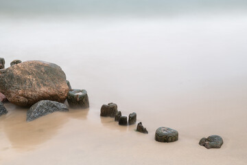 Sandy beach with old wooden breakwater and stones. Long exposure shot.