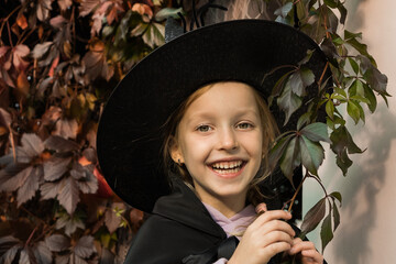 Portrait of little cute girl in witch costume and hat for halloween on fall autumn leaves background. Happy Halloween.