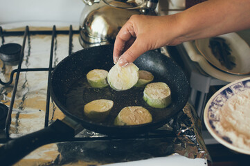 Hands fry green zucchini in flour in frying pan on gas stove
