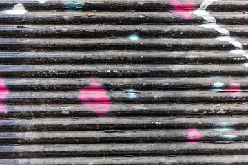Old black with colorful spots empty metal roller shutter door background texture. Copy space