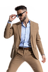 stylish caucasian man in brown suit with open collar shirt fixing sunglasses