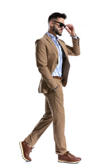 side view of young smart casual man adjusting glasses and walking