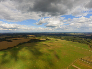 A view from the Drone of an agricultural field and the sky with clouds. A sunny autumn day landscape. The shadows from the clouds on the ground. Haystacks.