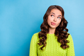 Photo of lovely young lady curly hairdo uncertain look empty space wear trendy fall green knitted jumper isolated on blue color background