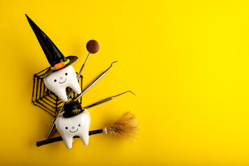 dental concept. tooth figurine in halloween costume and dental tools. pumpkins and a broom. on a yellow background
