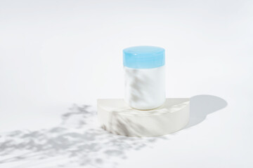 Cosmetic jar for cream on white podium and spring flowers shadows. Template for branding identity for cosmetics produce.