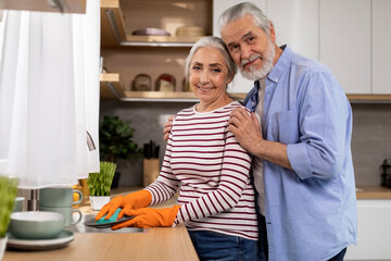 Senior Husband And Wife Washing Dishes In Kitchen And Smiling At Camera