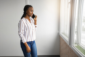 young african woman calling on mobile phone near window