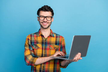 Photo of cheerful positive handsome man in spectacles wear plaid shirt holding laptop online meeting isolated on blue color background