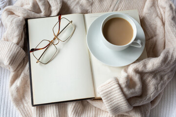 An open book with blank pages and a mug of cocoa on a warm sweater