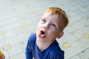 little red-haired boy laughing and grimacing on the street in summer - obrazy, fototapety, plakaty