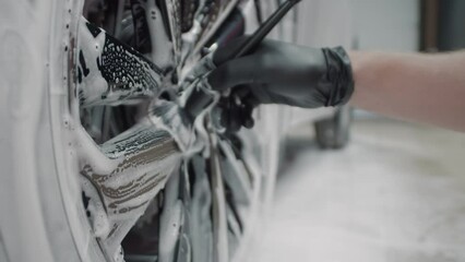 Closeup of a hand in black protective gloves using specialized car detailing brush to clean the rim of a wheel during a luxury car wash