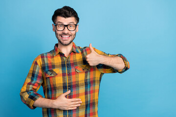 Naklejka premium Photo of satisfied cheerful positive guy in spectacles wear checkered shirt showing like arm on stomach isolated on blue color background