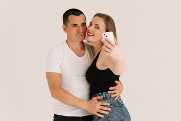 Two adults, a man and a woman in casual clothes, look into the phone, type a message, take a selfie using a mobile phone and technology on a white isolated background. Selective focus. Place for text