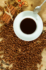 White cup of black coffee and coffee beans on burlap sack with nuts and cinnamon