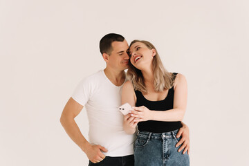 Two adults, a man and a woman in casual clothes, look into the phone, type a message, take a selfie using a mobile phone and technology on a white isolated background. Selective focus. Place for text