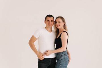 Fototapeta premium Two adults, a man and a woman in casual clothes, smile and look at the camera on a white isolated background. Selective focus. Space for text. A couple in love hugging